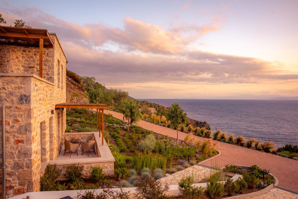 Stone-built suites at Sampatiki with a pergola terrace and planted slope above the Aegean at sunset